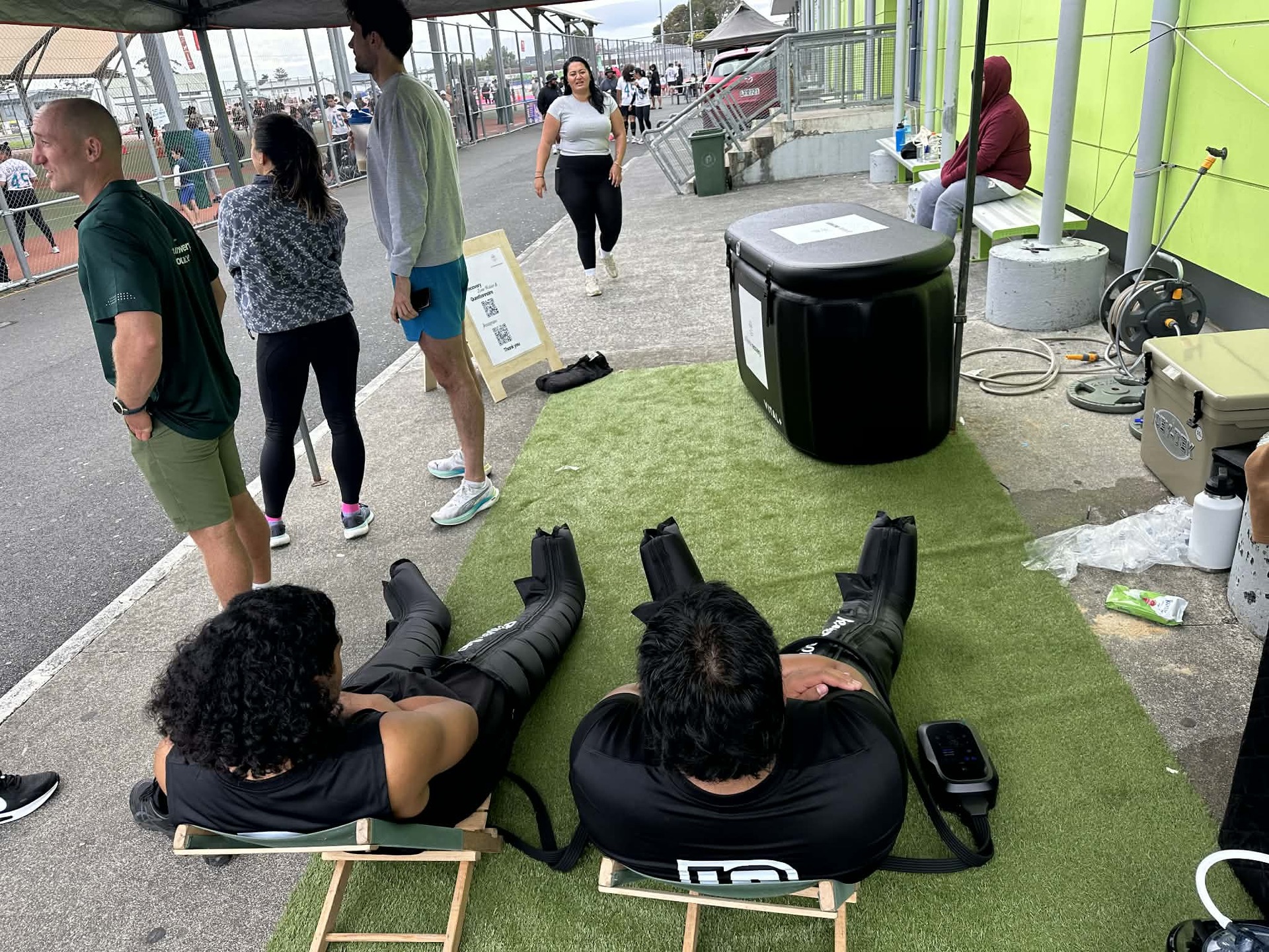 Teammates gathered around the ice bath under the At Home Recovery tent