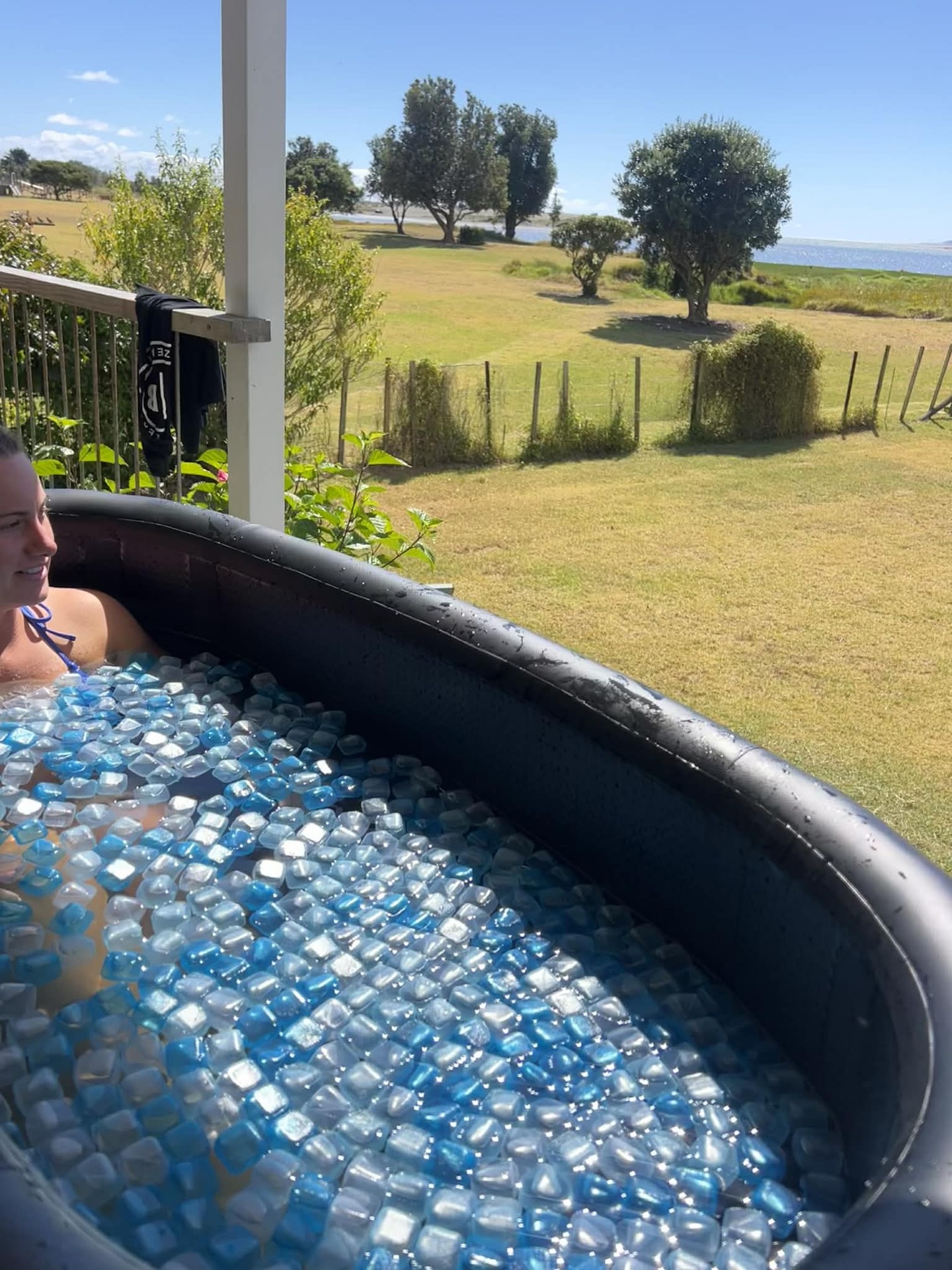 Someone relaxing in an ice bath full of blue ice cubes, looking out over a paddock